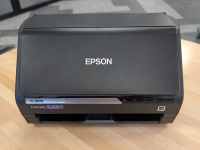 Black Epson FastFoto FF-680W machine sitting on a wooden table, with a grey rug in the background.