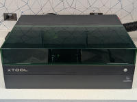 A black XTool S1 Laser Engraver machine sitting on a white countertop with white and grey backsplash behind the machine.